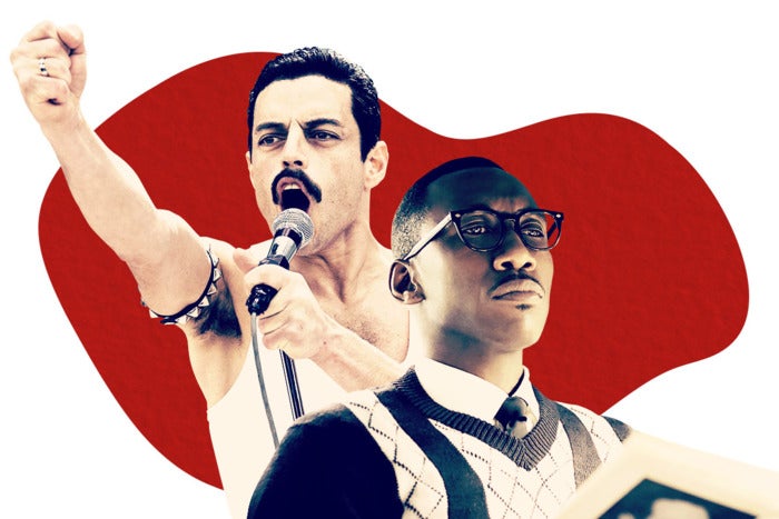 Caucasian man with a mustache wearing a white tank top, speaking into a mic with fist raised. Black man in a sweater, white dress shirt and black tie and wide-rimmed black glasses looking into the distance.